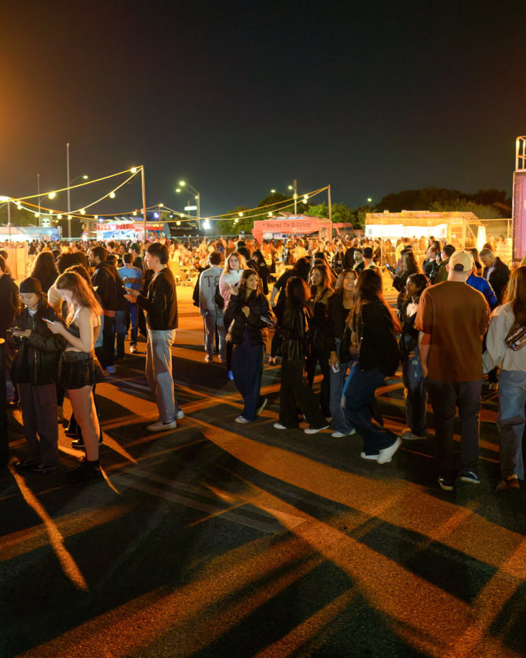 A crowd having fun in the parking lot of Tate McRae's album release party. In the distance are several food trucks catering to guests.