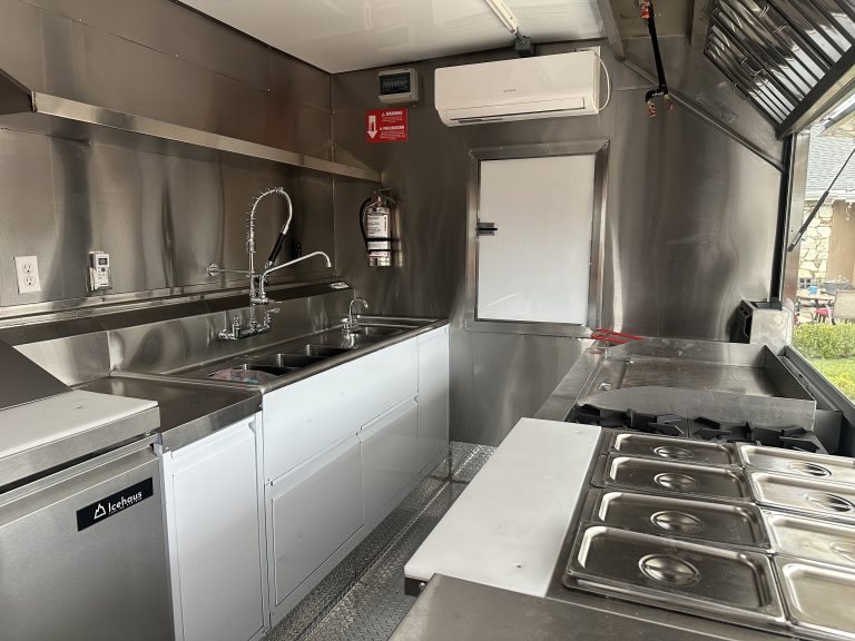 A wide shot of the interior of a food trailer. It has a three compartment sink and other tools.