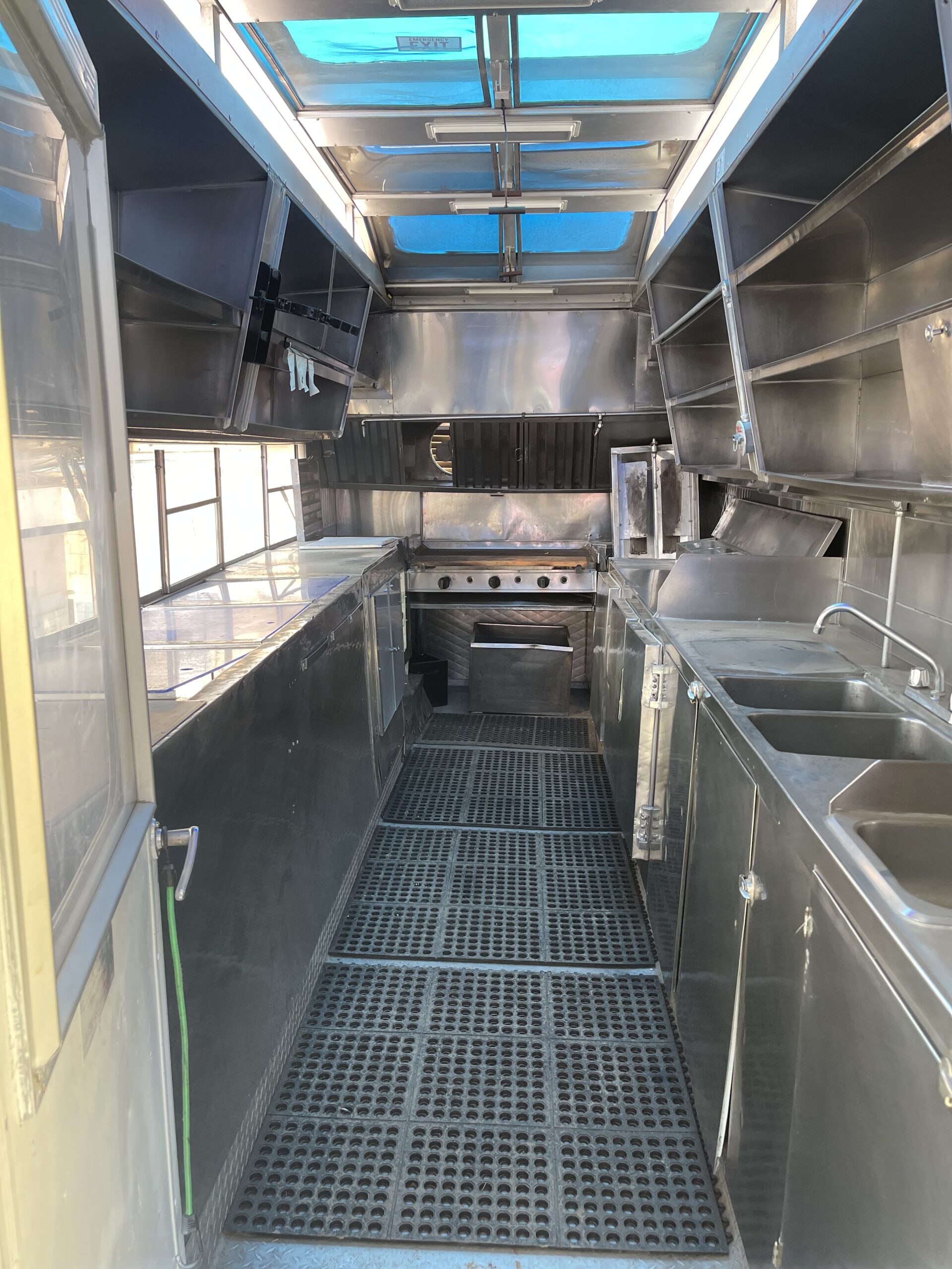 An interior shot of the food truck Rooster Gallo, from the entrance looking in. Contains a stove, compartment sink, shelving, and more.
