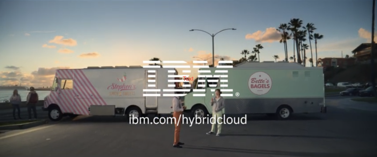 A wide shot on a road at sunset. Two food trucks are parked together, blocking the road for the AD. Standing in front of the food trucks are the drivers discussing. In front of them is the IBM logo, followed by a link to IBM’s hybrid cloud.